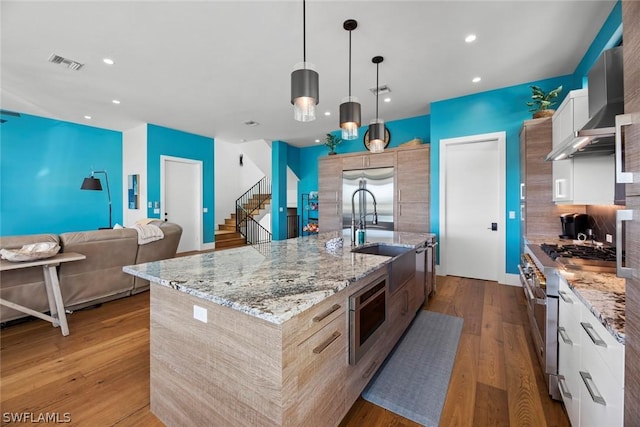 kitchen with a spacious island, white cabinetry, built in appliances, decorative light fixtures, and wall chimney range hood