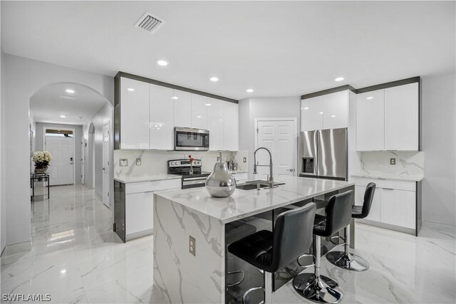 kitchen featuring stainless steel appliances, white cabinets, a center island with sink, and sink