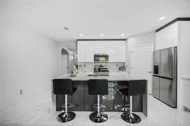 kitchen with appliances with stainless steel finishes, white cabinetry, sink, and a kitchen breakfast bar