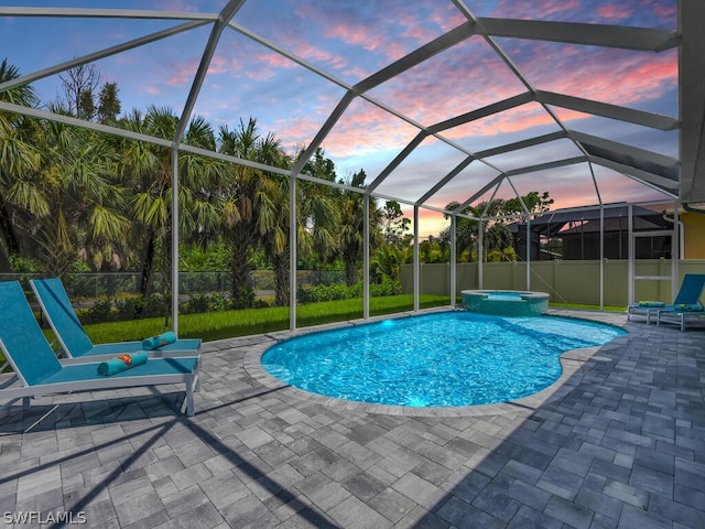 pool at dusk with glass enclosure, a patio area, and an in ground hot tub