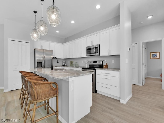 kitchen featuring sink, hanging light fixtures, a center island with sink, white cabinets, and appliances with stainless steel finishes