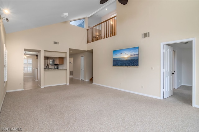 unfurnished living room with ceiling fan, high vaulted ceiling, and light carpet