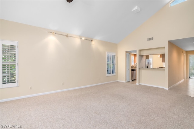 unfurnished living room featuring high vaulted ceiling and light colored carpet