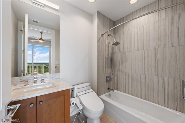 full bathroom with ceiling fan, toilet, vanity, and tiled shower / bath