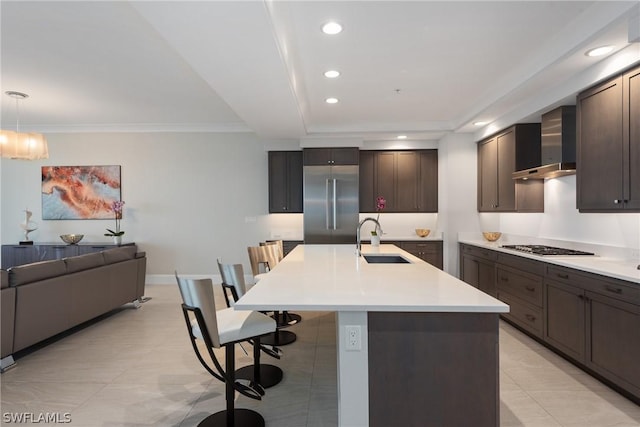 kitchen featuring sink, wall chimney exhaust hood, hanging light fixtures, a kitchen breakfast bar, and a kitchen island with sink