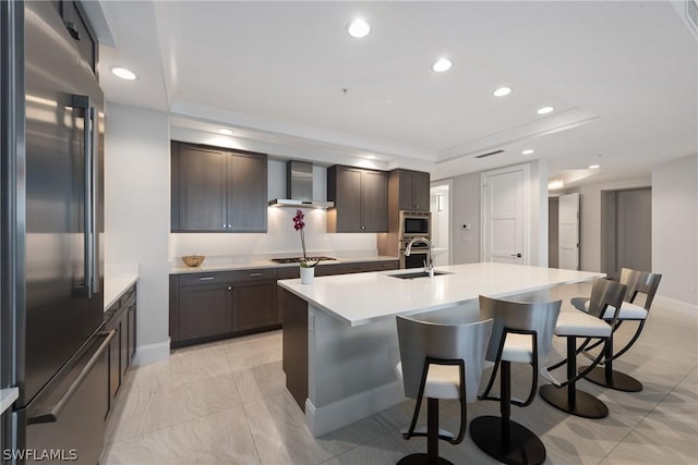 kitchen with a kitchen island with sink, sink, wall chimney exhaust hood, dark brown cabinetry, and stainless steel appliances