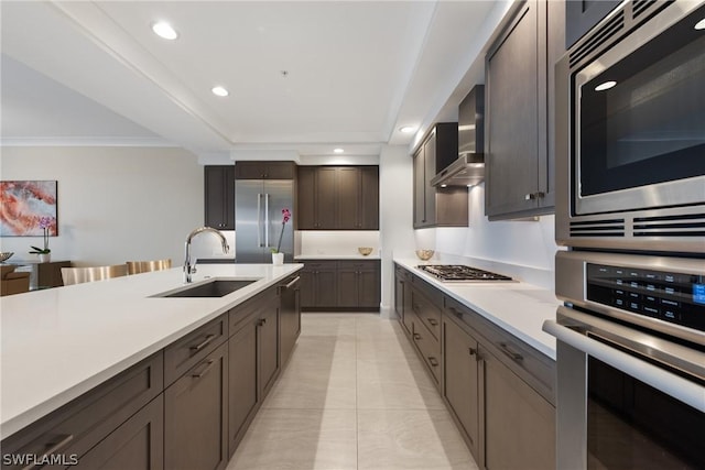 kitchen featuring wall chimney range hood, sink, built in appliances, light tile patterned floors, and dark brown cabinetry