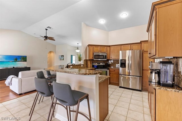 kitchen with appliances with stainless steel finishes, dark stone counters, ceiling fan, and light tile floors