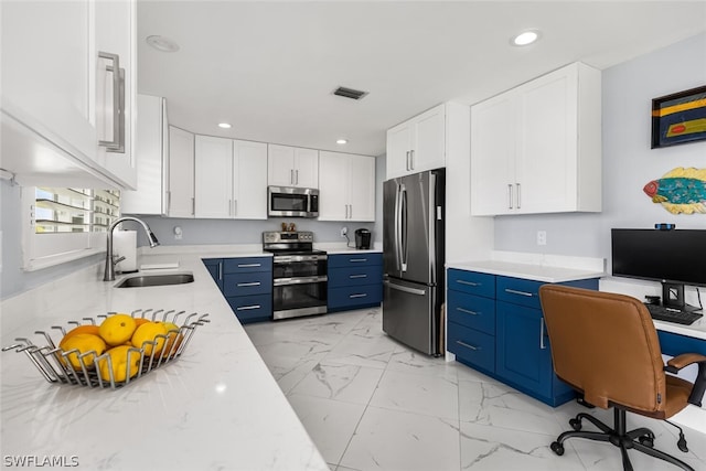 kitchen with blue cabinetry, sink, white cabinets, built in desk, and appliances with stainless steel finishes