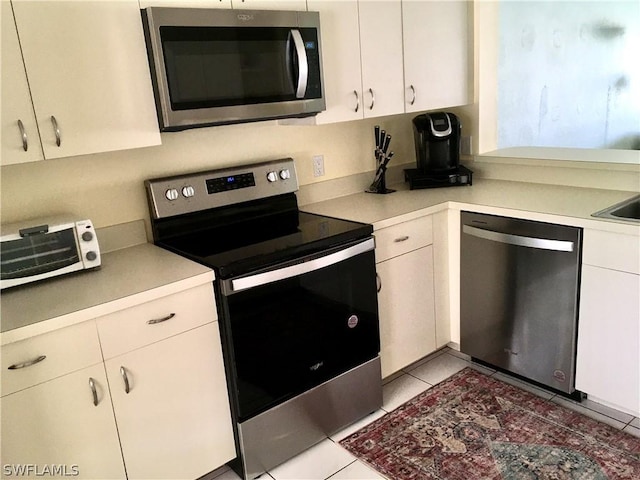 kitchen with light tile patterned flooring, white cabinets, and stainless steel appliances