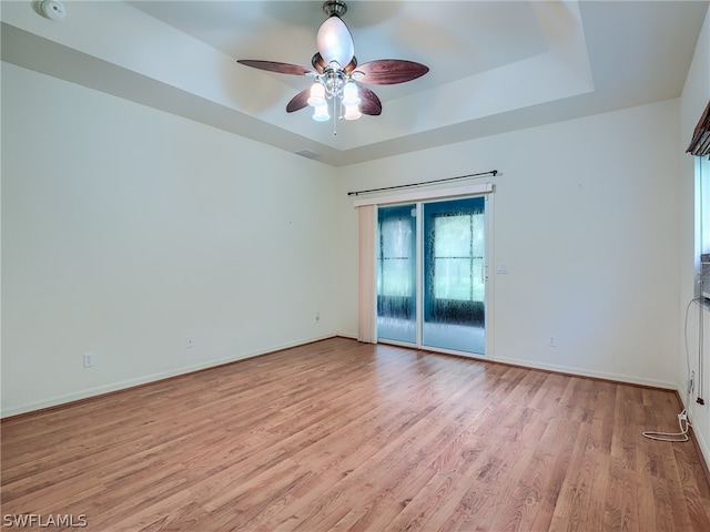 empty room featuring light wood-type flooring, ceiling fan, and a raised ceiling