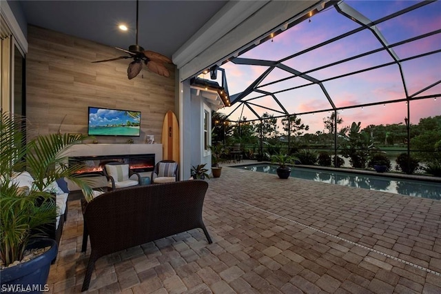 view of patio with an outdoor living space, glass enclosure, and ceiling fan