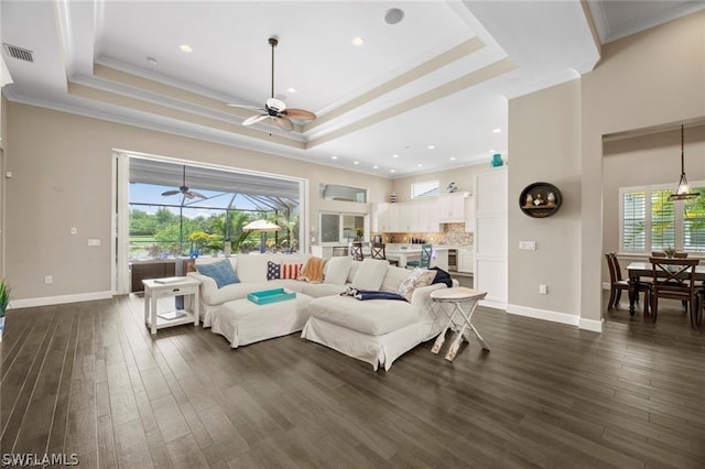 living room featuring dark hardwood / wood-style flooring, a raised ceiling, ornamental molding, and a wealth of natural light