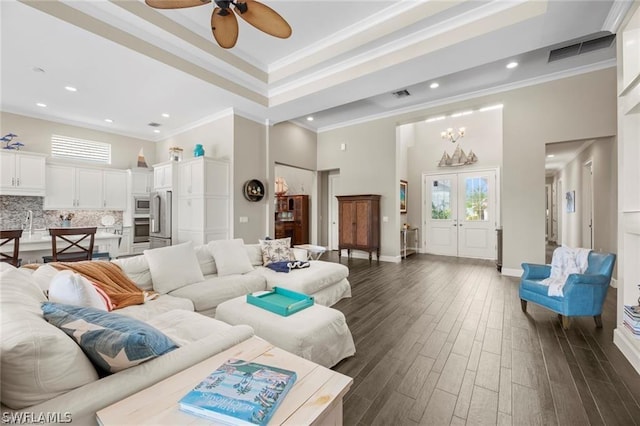 living room with ceiling fan with notable chandelier, a towering ceiling, crown molding, and dark wood-type flooring