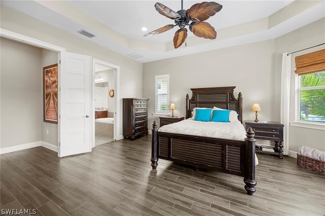 bedroom featuring dark hardwood / wood-style flooring, a raised ceiling, ensuite bath, and ceiling fan