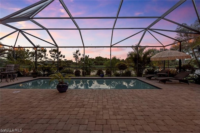 pool at dusk featuring glass enclosure and a patio