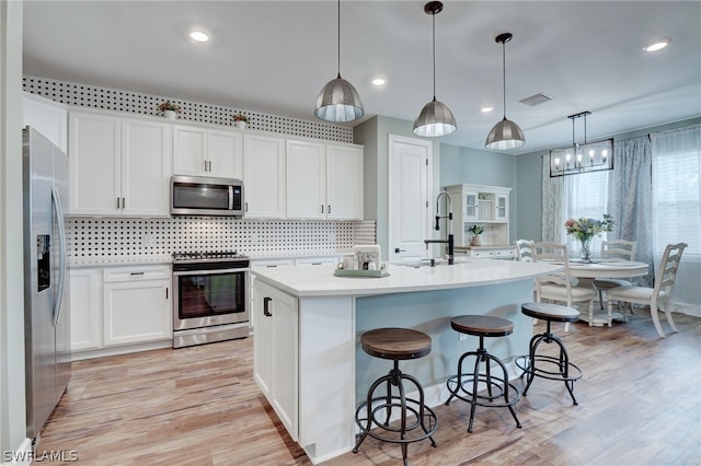 kitchen featuring sink, stainless steel appliances, decorative light fixtures, a center island with sink, and white cabinets