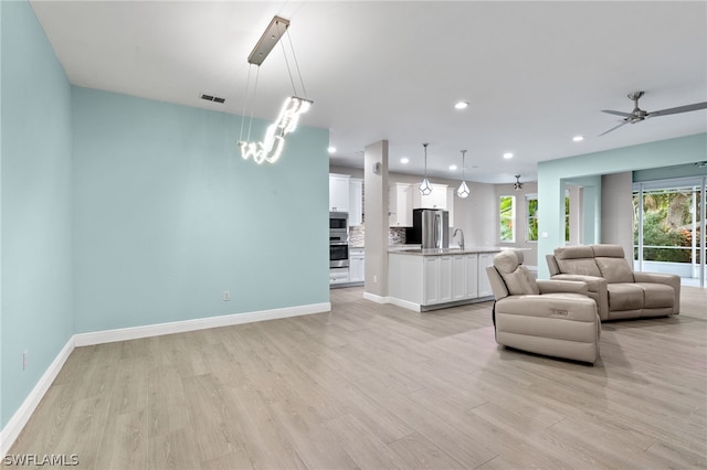 living room featuring sink, ceiling fan with notable chandelier, and light wood-type flooring