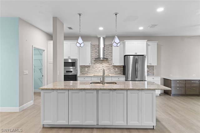 kitchen with wall chimney exhaust hood, stainless steel appliances, sink, a center island with sink, and white cabinetry