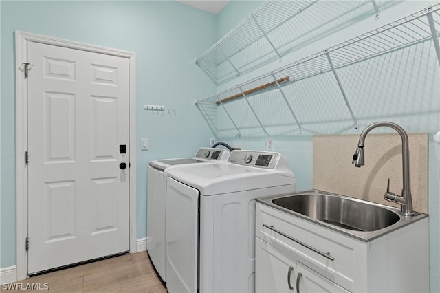 washroom featuring sink, light hardwood / wood-style flooring, cabinets, and washing machine and clothes dryer