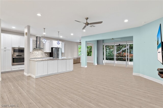 kitchen with appliances with stainless steel finishes, tasteful backsplash, wall chimney range hood, white cabinetry, and hanging light fixtures