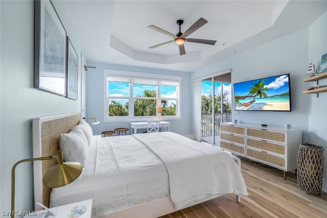 bedroom featuring access to outside, light hardwood / wood-style flooring, a raised ceiling, and ceiling fan