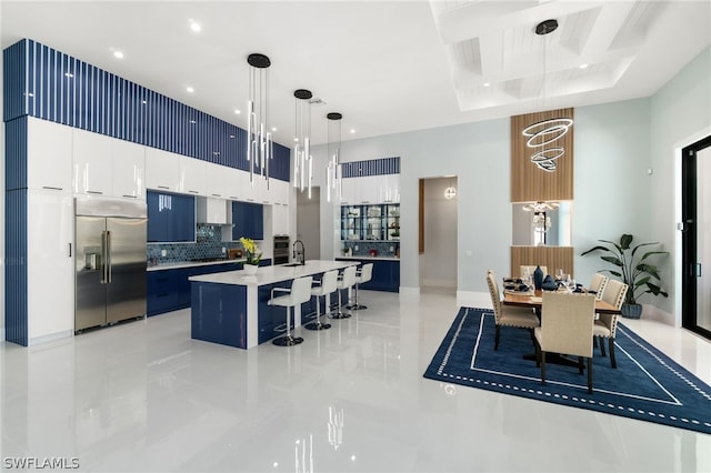 kitchen with built in fridge, pendant lighting, white cabinets, a kitchen bar, and a kitchen island with sink