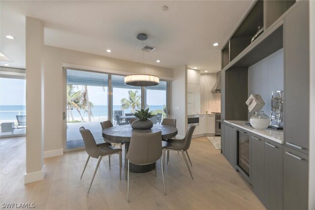 dining area featuring a water view, light hardwood / wood-style flooring, and beverage cooler