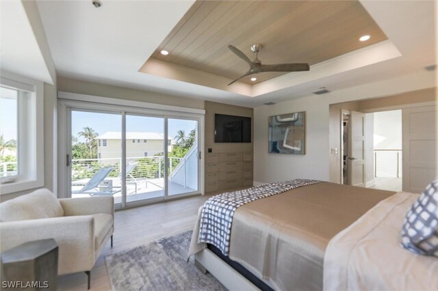 bedroom featuring ceiling fan, light hardwood / wood-style floors, a tray ceiling, and access to outside