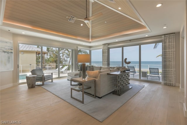 living room with a tray ceiling, hardwood / wood-style floors, a water view, and wood ceiling