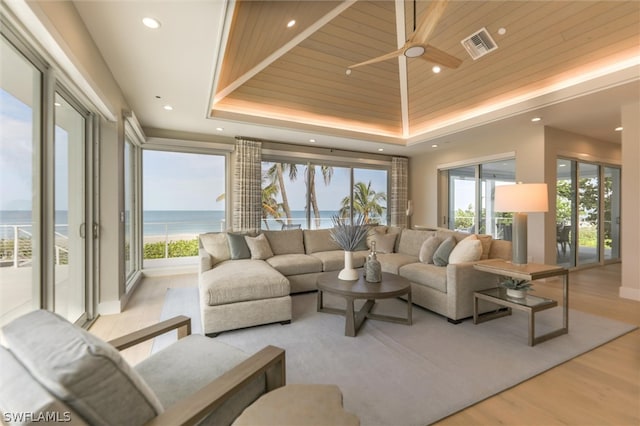 living room with ceiling fan, light hardwood / wood-style floors, a tray ceiling, a water view, and wooden ceiling