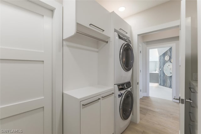 laundry area featuring stacked washer / drying machine, cabinets, and light wood-type flooring