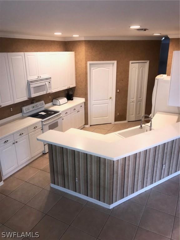 kitchen featuring white cabinetry, kitchen peninsula, sink, white appliances, and dark tile patterned flooring