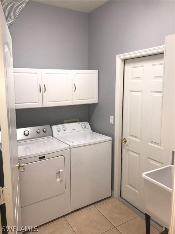 clothes washing area featuring washer and dryer, light tile patterned floors, and cabinets