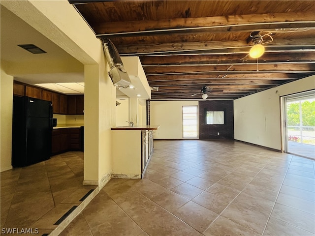 basement featuring ceiling fan, black refrigerator, light tile patterned floors, and a wealth of natural light