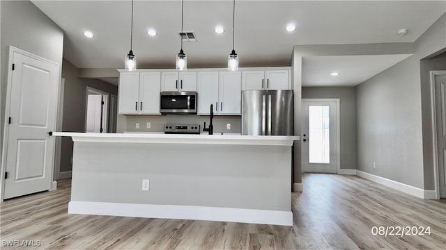 kitchen with hanging light fixtures, stainless steel appliances, white cabinetry, and a kitchen island with sink