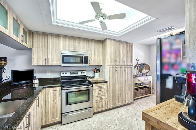 kitchen featuring light brown cabinets, dark stone countertops, light tile patterned floors, a tray ceiling, and stainless steel appliances