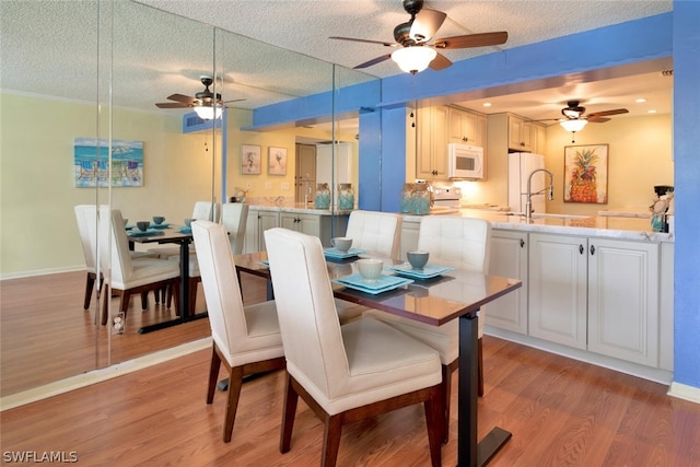 dining room with light wood-type flooring, a textured ceiling, ceiling fan, and sink