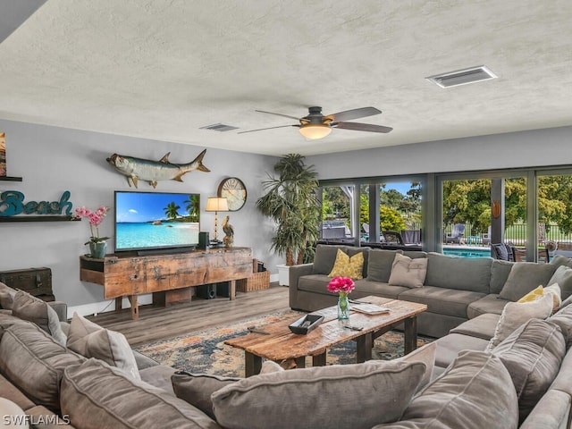 living area with a ceiling fan, a textured ceiling, visible vents, and wood finished floors