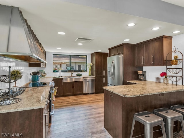 kitchen with light stone countertops, stainless steel appliances, light wood-type flooring, and custom exhaust hood