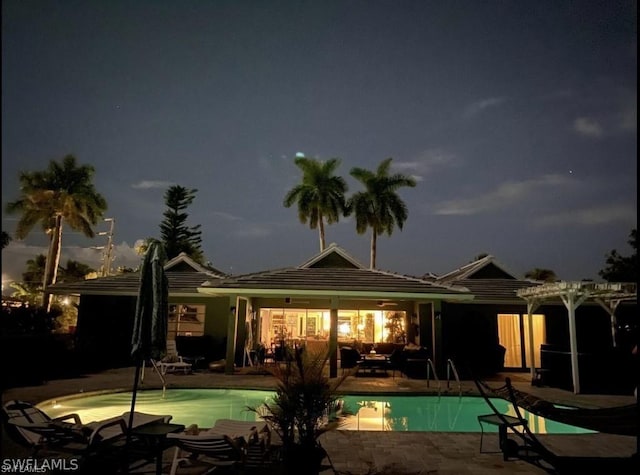 back of house at night featuring a patio and an outdoor pool