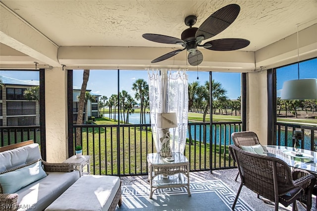 sunroom with ceiling fan and a water view