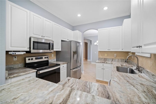 kitchen featuring arched walkways, a sink, appliances with stainless steel finishes, light stone countertops, and crown molding