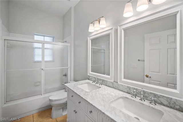 bathroom with bath / shower combo with glass door, a sink, toilet, and double vanity