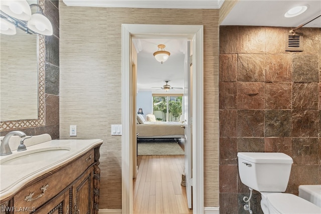 bathroom with ceiling fan, hardwood / wood-style floors, toilet, vanity, and tile walls