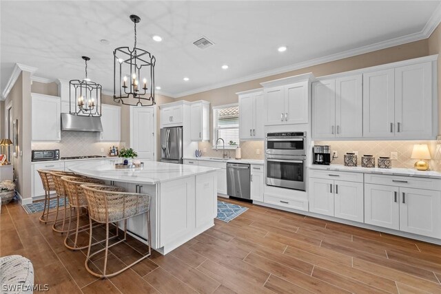 kitchen with a center island, appliances with stainless steel finishes, decorative light fixtures, white cabinetry, and extractor fan