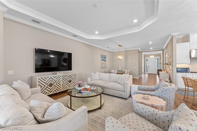 living room with a raised ceiling, light hardwood / wood-style flooring, and ornamental molding