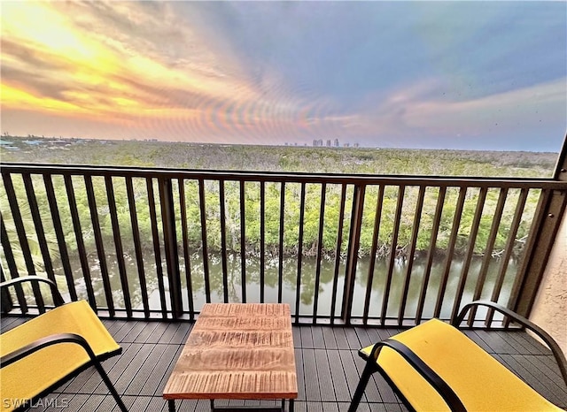 balcony at dusk featuring a water view