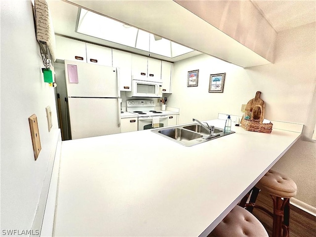 kitchen with sink, kitchen peninsula, white appliances, a breakfast bar, and white cabinets