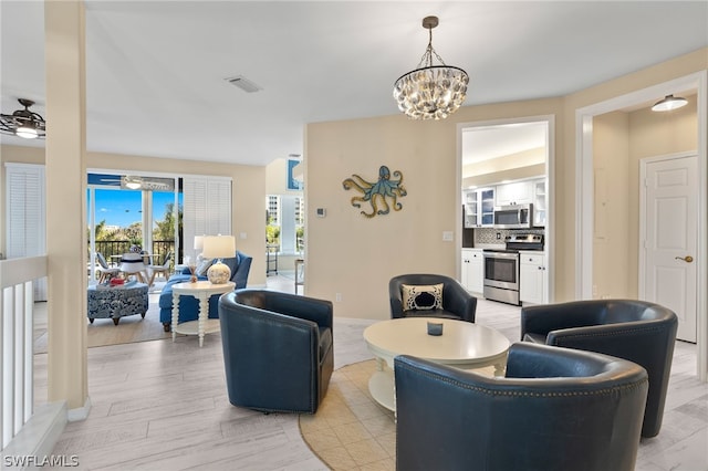 living room with light hardwood / wood-style floors and ceiling fan with notable chandelier